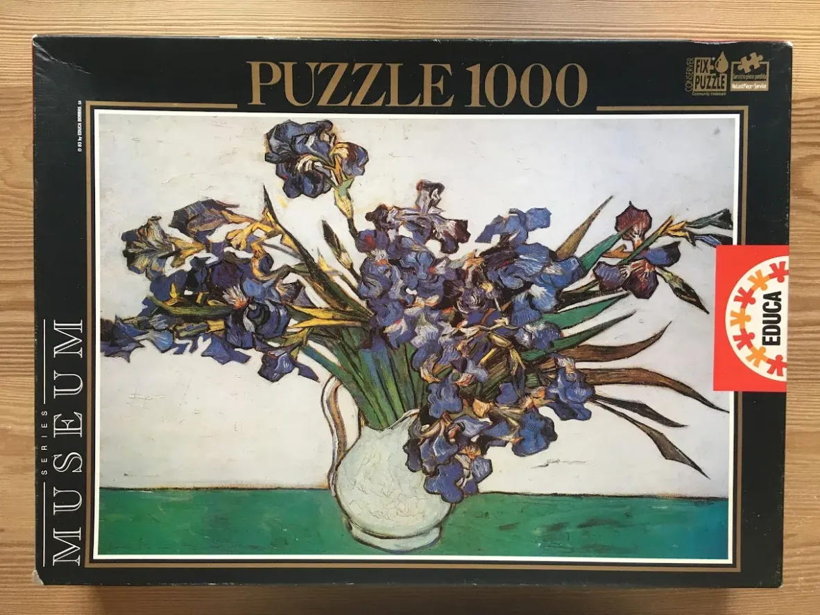 A still life painting by Vincent van Gogh of deep blue irises in a white pitcher against a plain background.