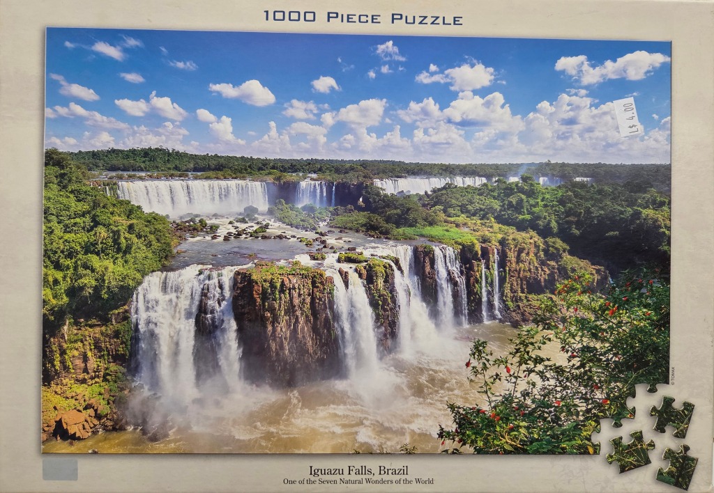 Panoramic view of the multi-tiered Iguazu Falls surrounded by lush jungle under a clear blue sky.