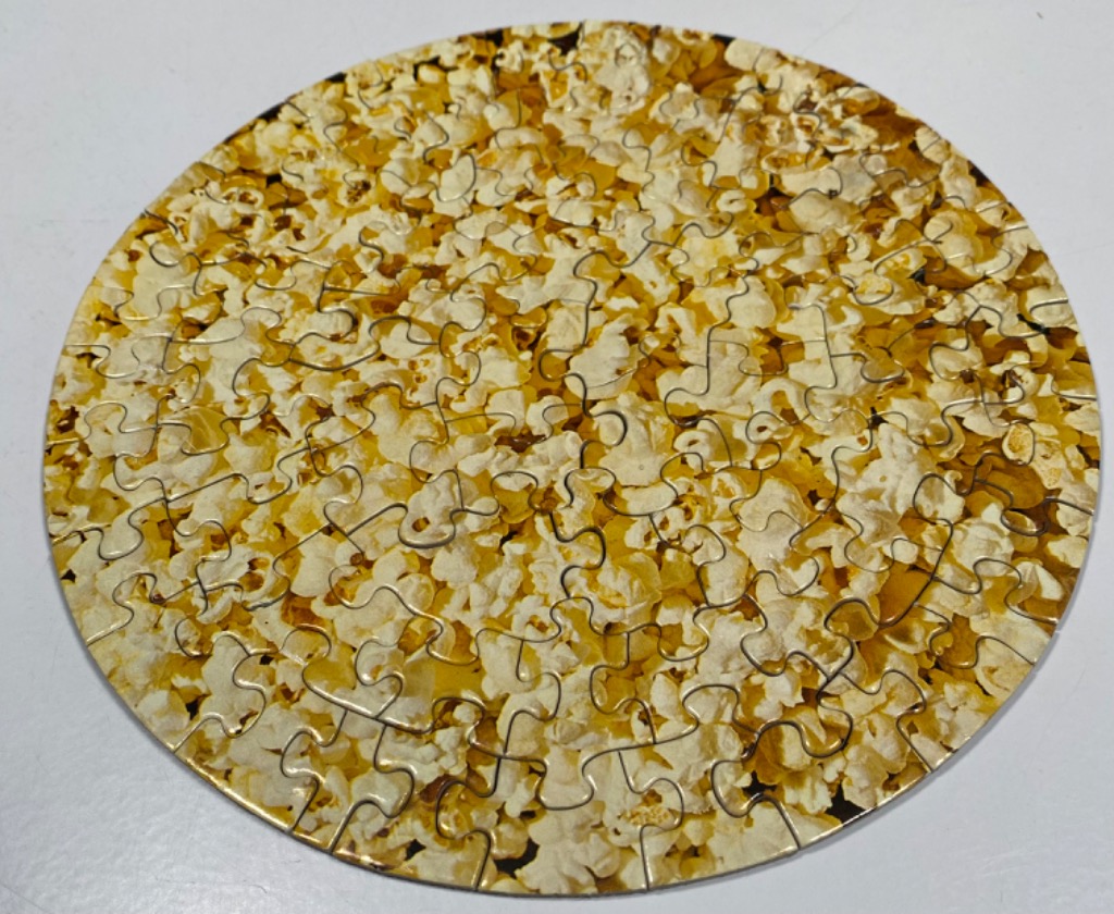 A circular image filled with a dense, overhead view of buttery popcorn.