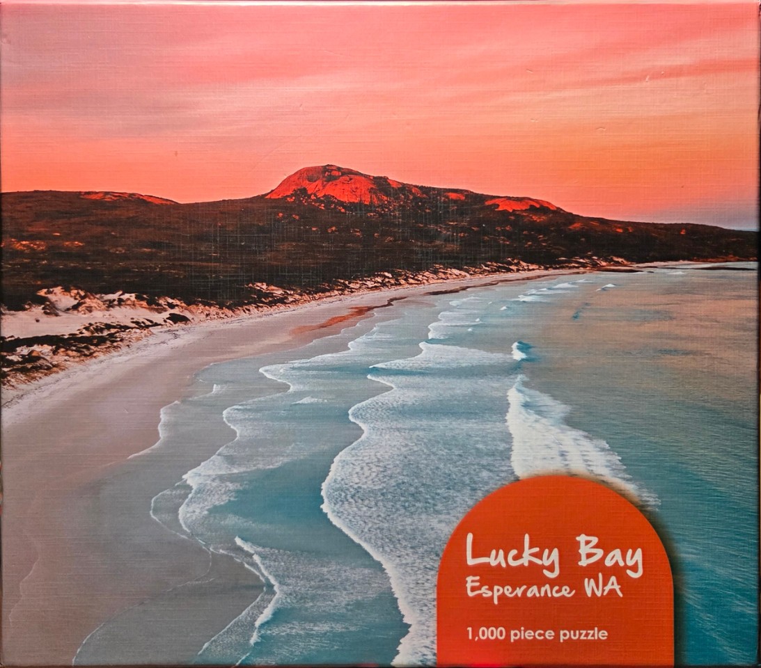 Aerial view of a coastal beach at sunset with a red-hued mountain in the background.