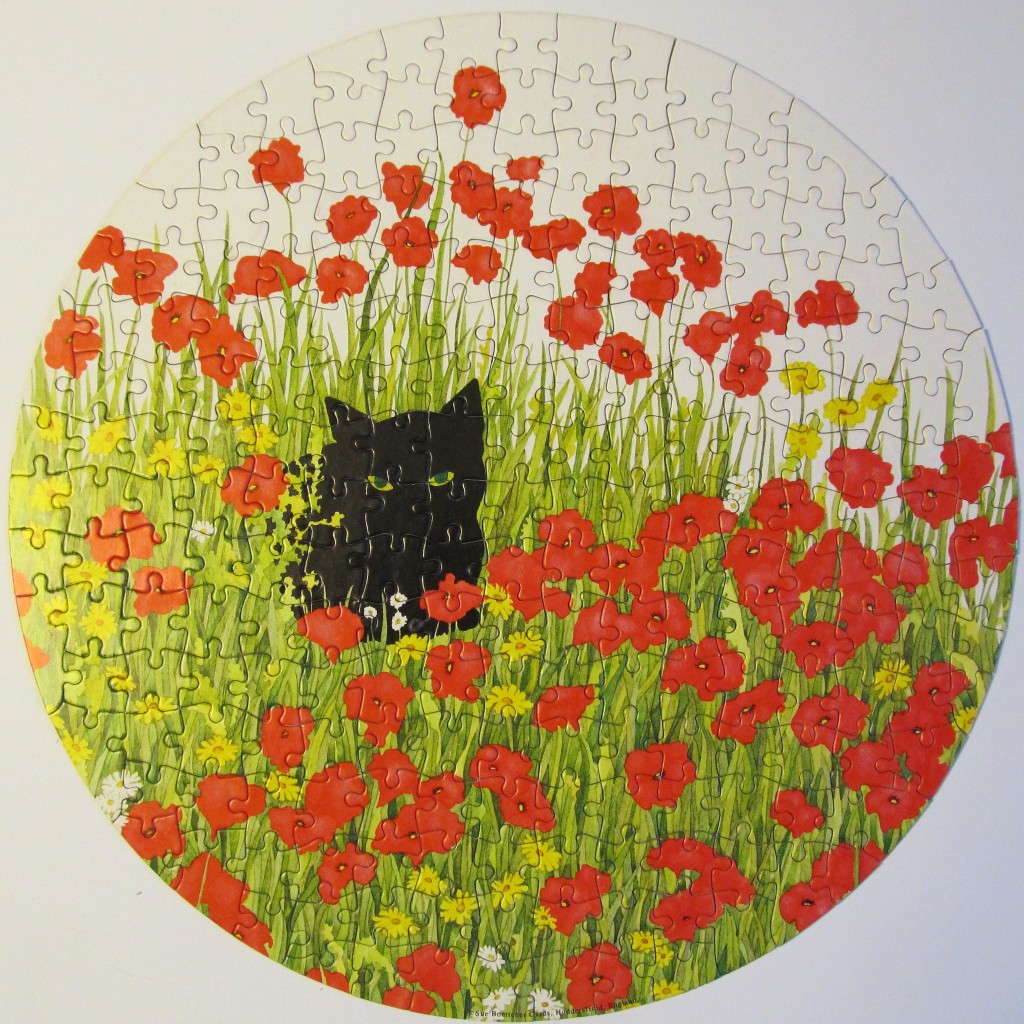 A black cat hiding in a meadow of red poppies and yellow wildflowers on a circular background.
