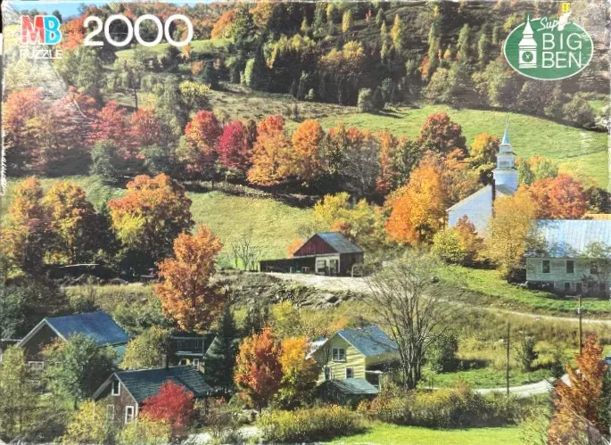 A peaceful rural landscape in autumn featuring a small white church and several houses nestled among colorful trees.