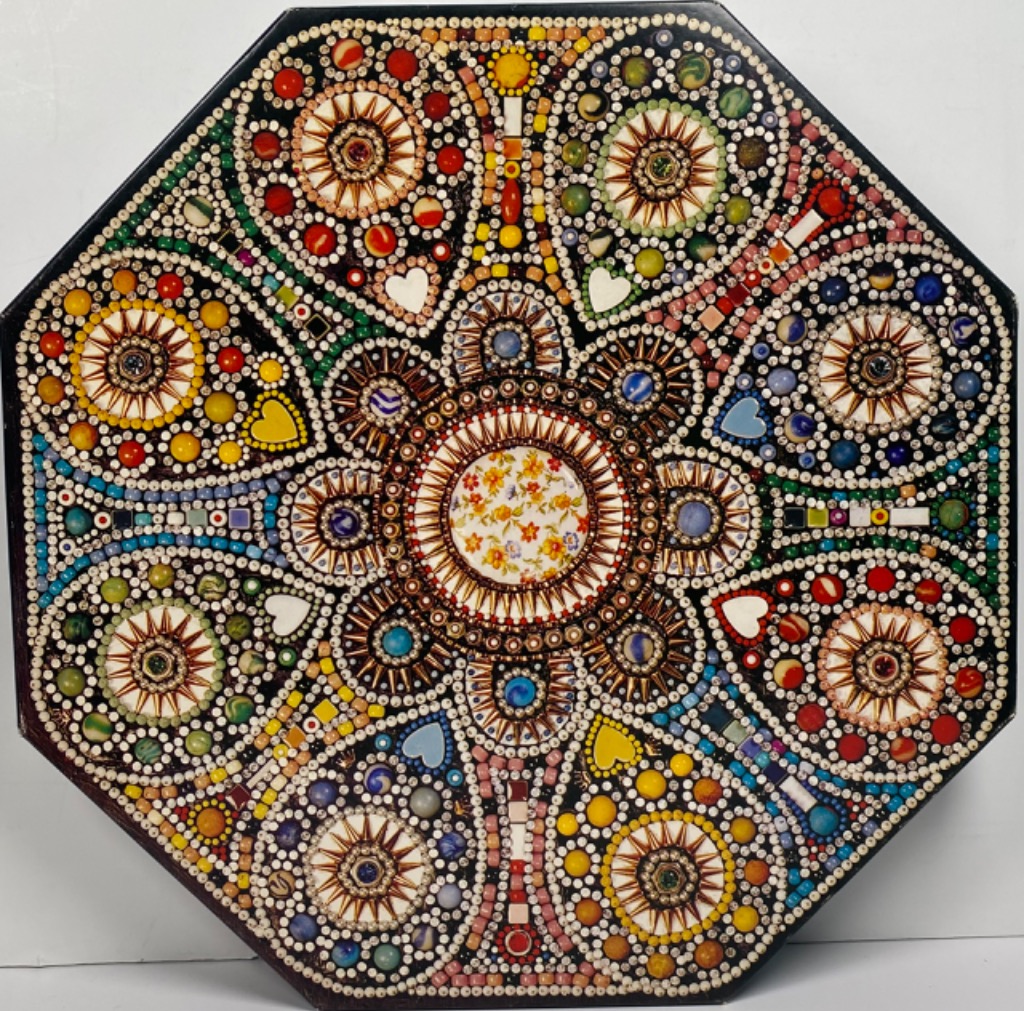 A complex octagonal mosaic design made of marbles, beads, and floral porcelain tiles.