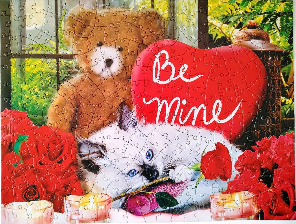 A teddy bear, fluffy kitten, and large heart with the text Be Mine surrounded by red roses and candles.