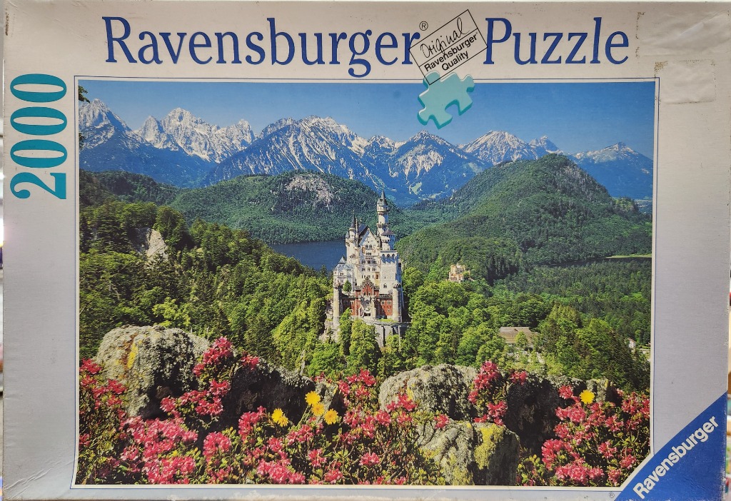 Neuschwanstein Castle surrounded by lush green forests, a dark blue lake, and snow-capped mountains.
