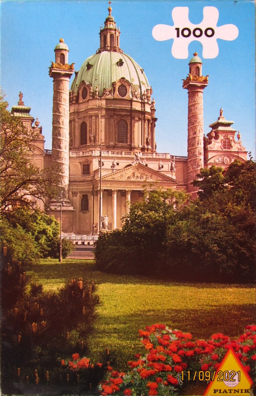A clear, sunny photograph of St. Charles Church in Vienna with its iconic green dome and two towering columns.