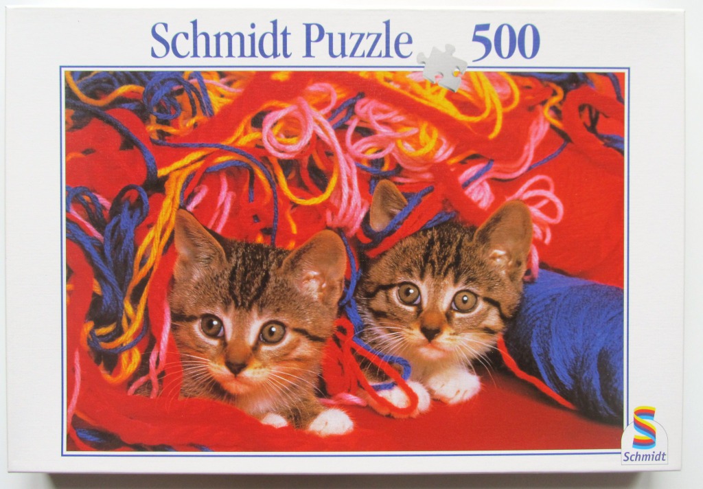 Two tabby kittens peeking through a tangled mess of colorful yarn