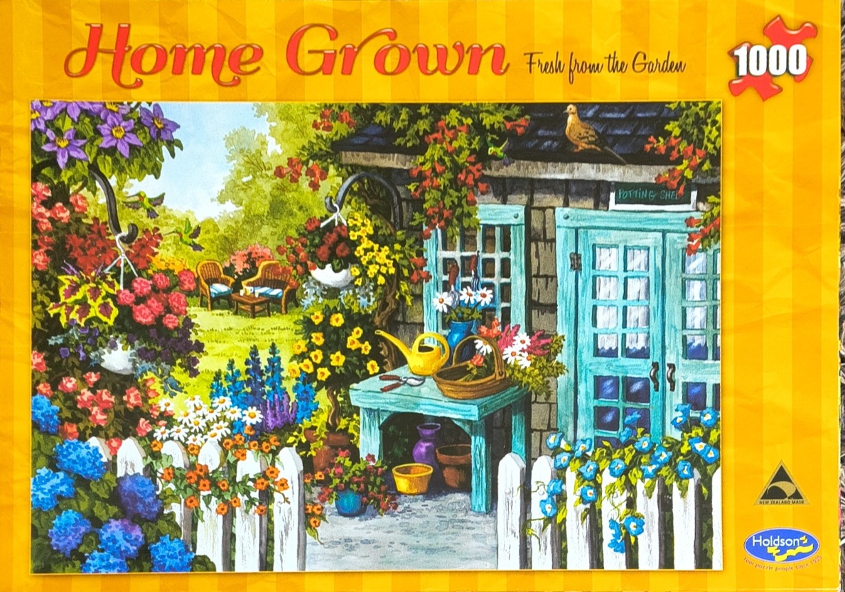 A lush, colorful garden scene featuring a blue potting shed, a white picket fence, and vibrant flower beds.