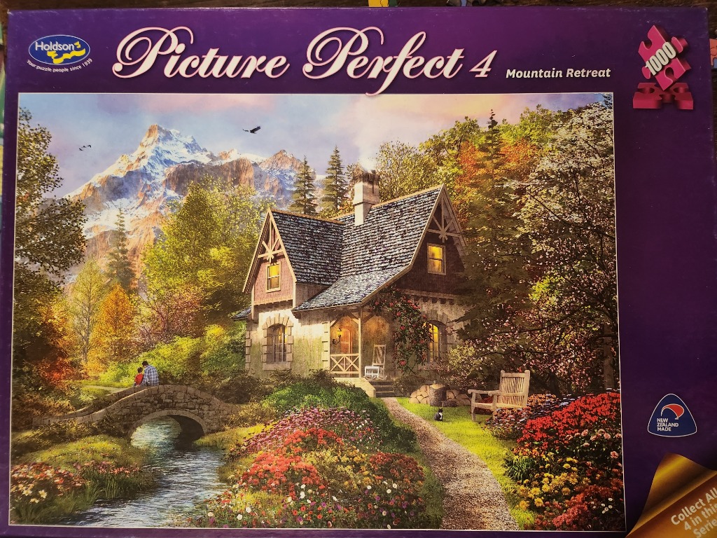 A serene stone cottage set in a vibrant autumnal garden with a small stone bridge over a stream and snow-capped mountains.