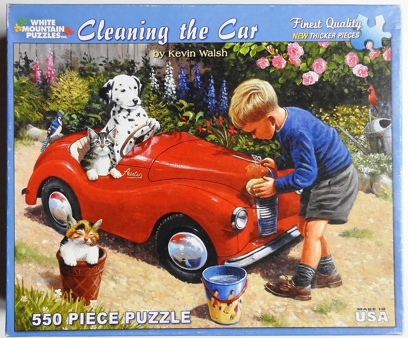 A boy washing a red toy car with a dog and two cats in a garden setting.
