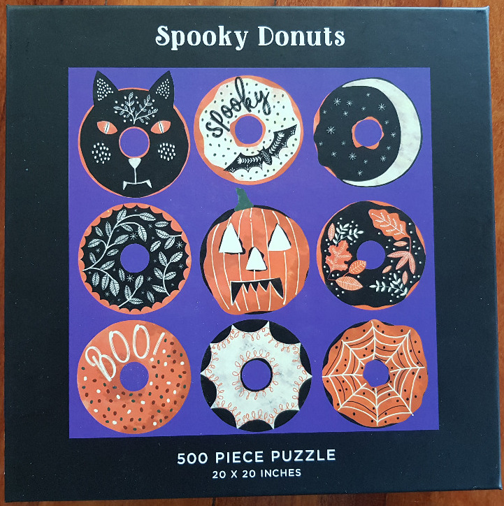 A whimsical illustration of nine Halloween-themed donuts arranged in a grid against a purple background.