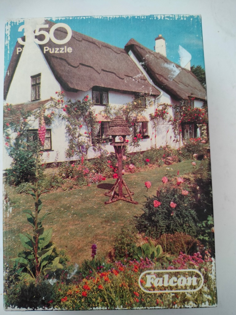 A traditional white cottage with a thatched roof surrounded by a flower-filled garden and a wooden bird table.