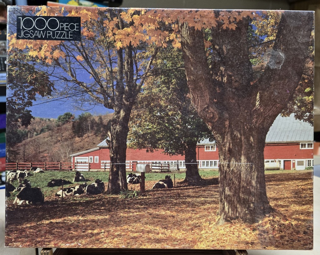 A red barn in a rural autumn setting with black and white cows grazing in a field under large, mature trees.