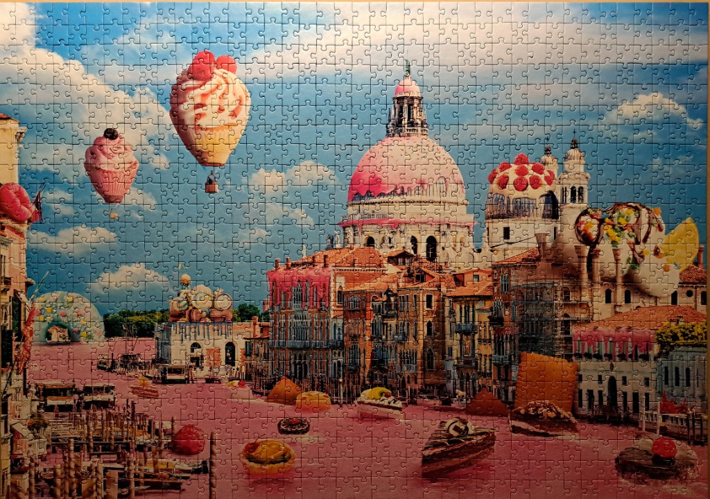 A whimsical surrealist scene of Venice covered in desserts, with a cupcake hot air balloon in a blue sky.