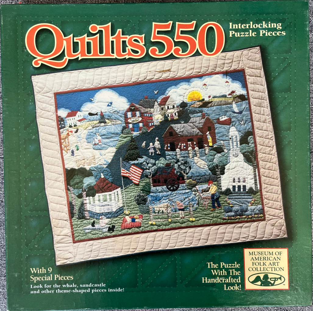 A quilt featuring a coastal New England town scene with a lighthouse, gazebo, houses, and an American flag.
