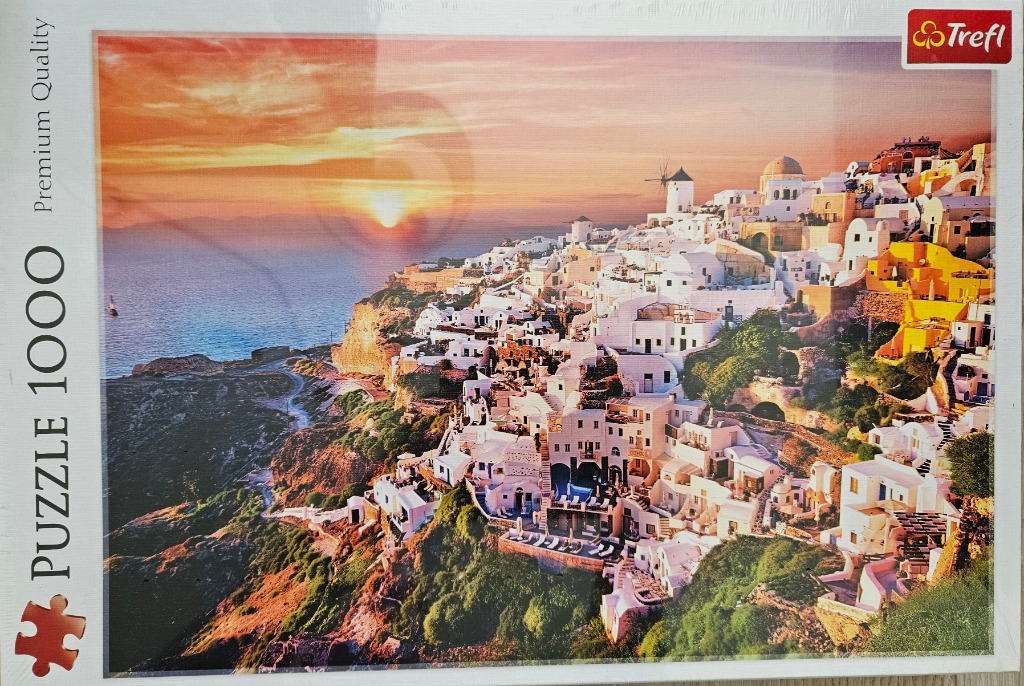 A photograph of Oia, Santorini, featuring white buildings on a cliff at sunset with an orange sky and blue sea.