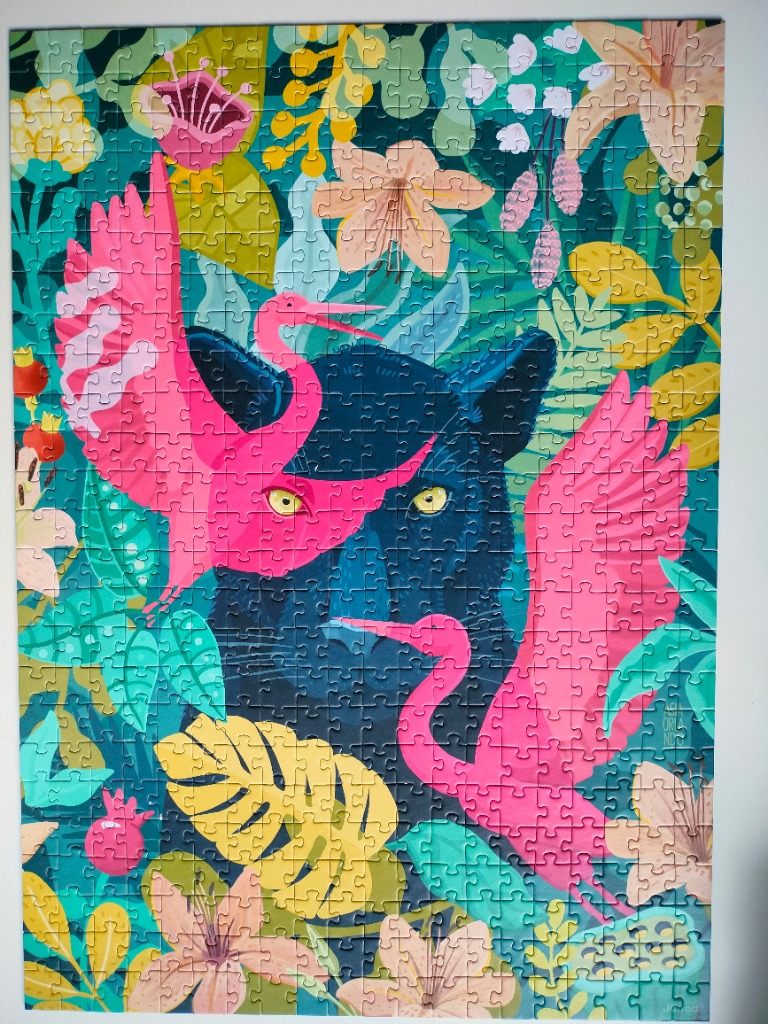 A black panther surrounded by tropical flowers and two bright pink birds in a lush jungle setting.