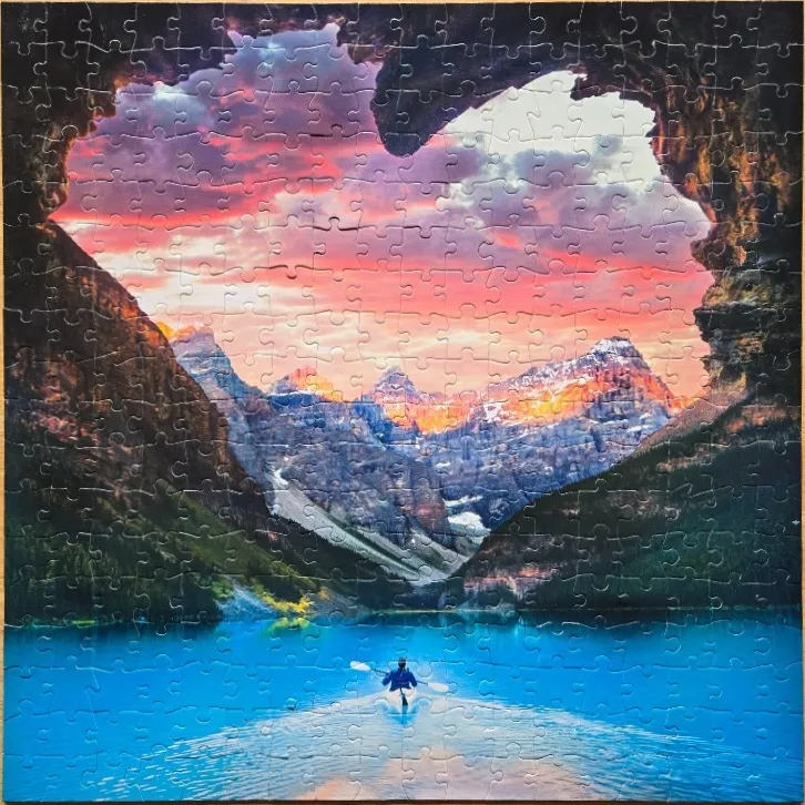 A kayaker on a bright blue glacial lake, viewed through a natural heart-shaped cave opening at sunset.