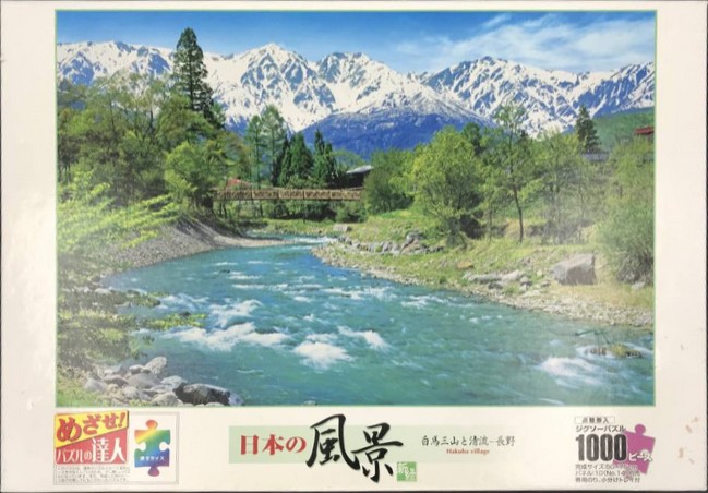 A clear mountain stream flowing through a lush green valley toward snow-capped peaks in the Japanese Alps.