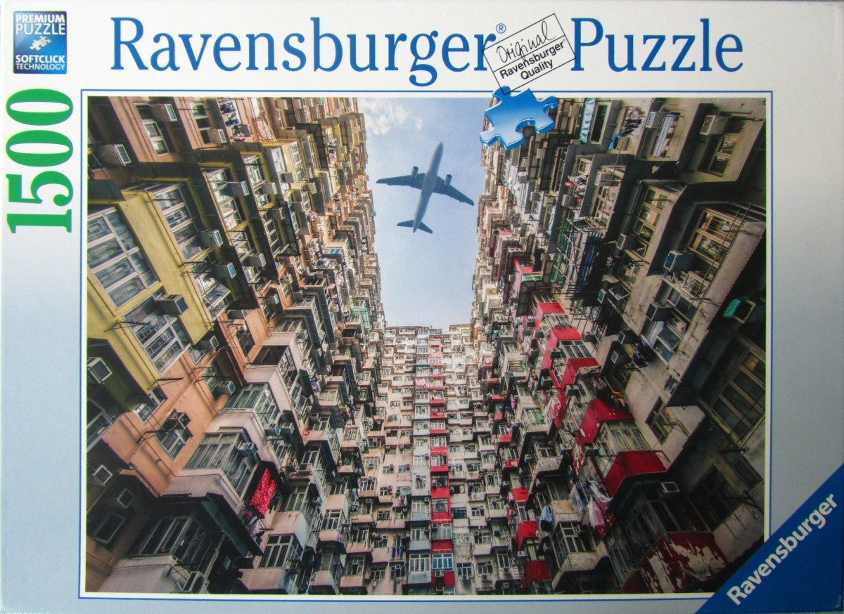 A low-angle photograph looking up at dense high-rise apartment buildings in Hong Kong with an airplane flying overhead.