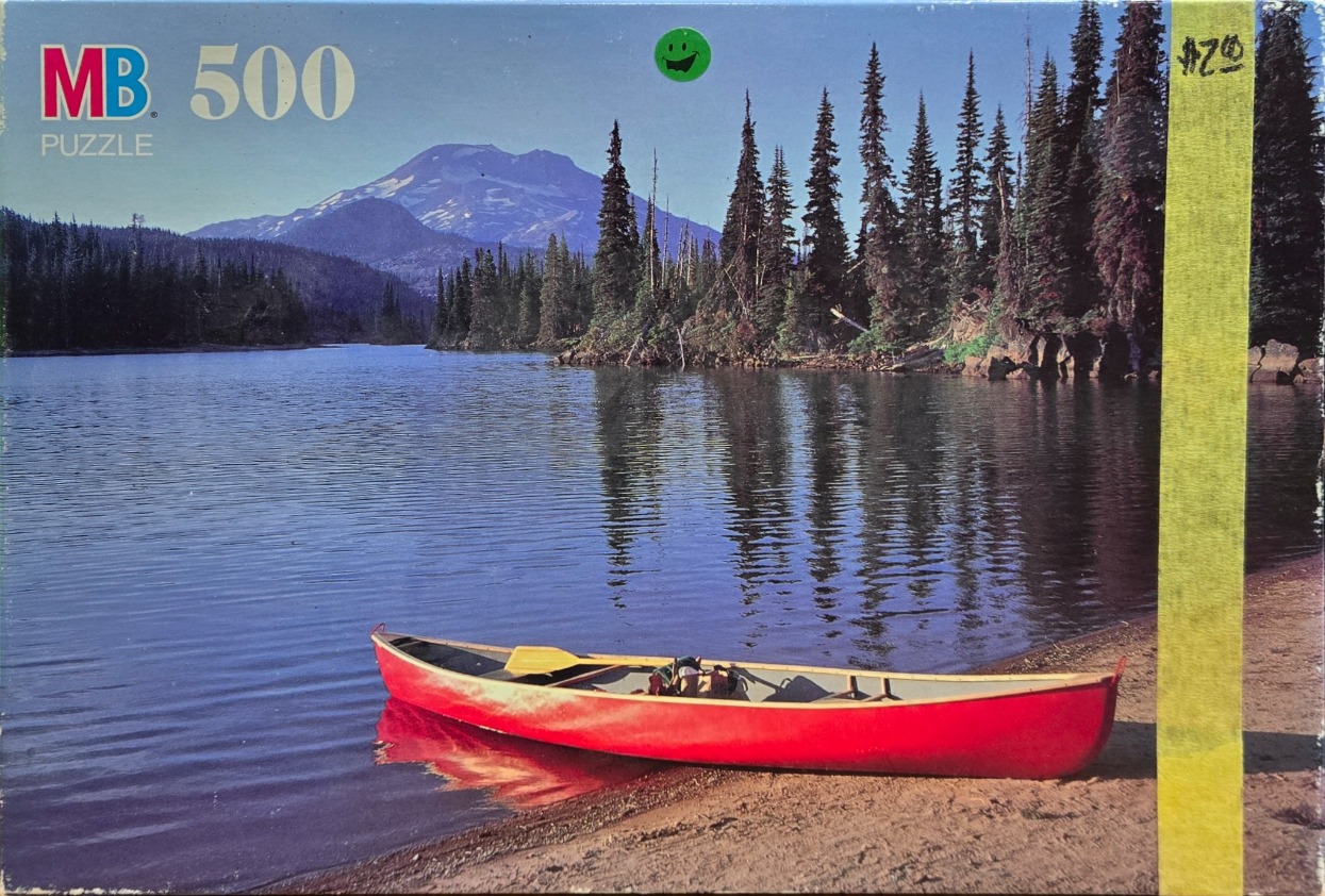 A bright red canoe resting on a sandy shore of a calm lake with a snow-capped mountain in the distance.