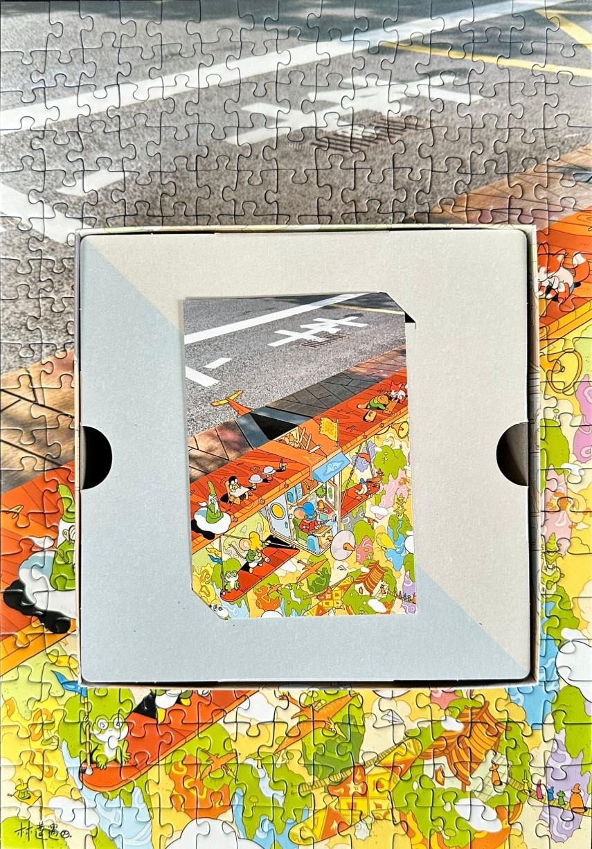 A whimsical illustration of tiny animals in a complex landscape nestled inside a box frame on a road surface.
