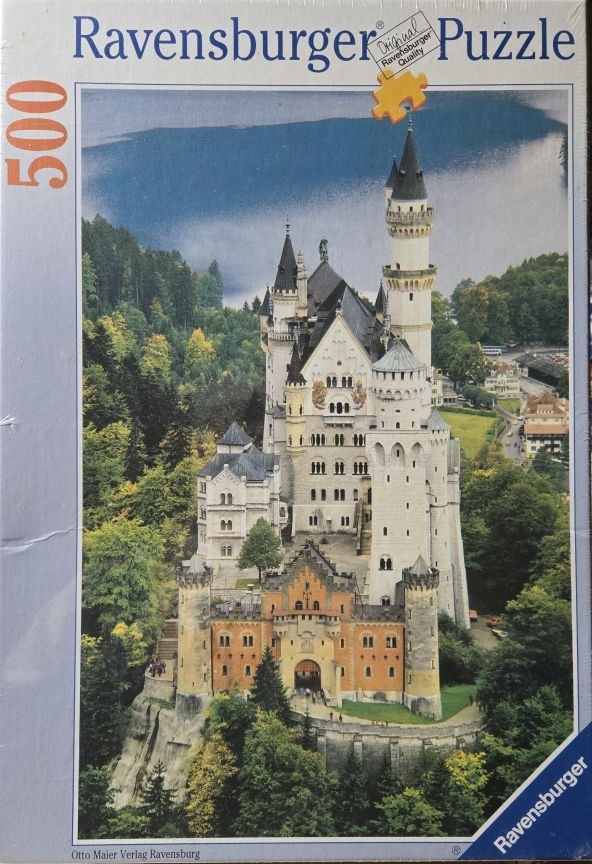 A photograph of Neuschwanstein Castle nestled in a lush, green forest with a mountain lake in the distance.