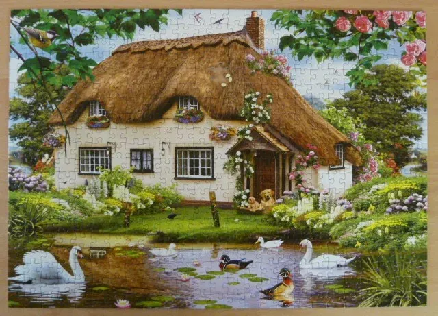 A thatched cottage with a pond featuring swans and ducks in a lush garden setting.