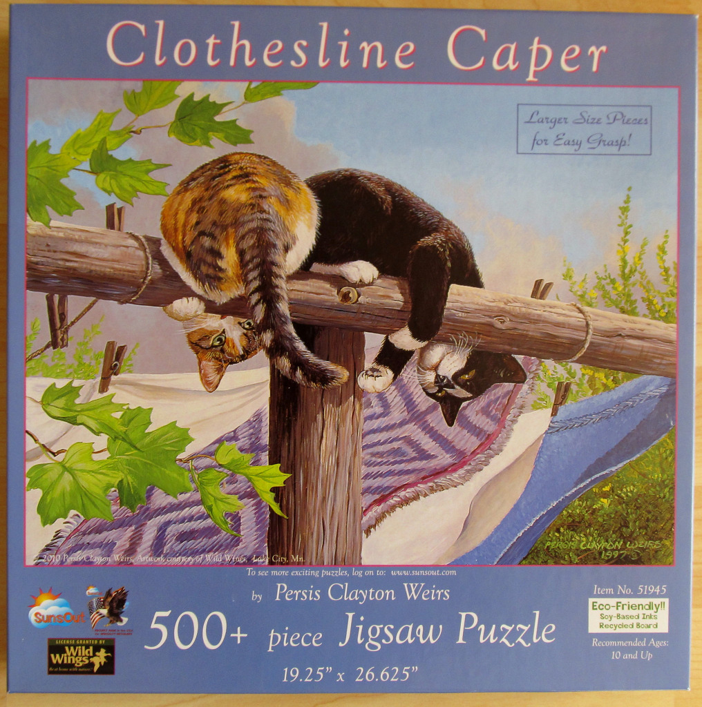 Two cats draped over a rustic wooden clothesline post with laundry hanging below.