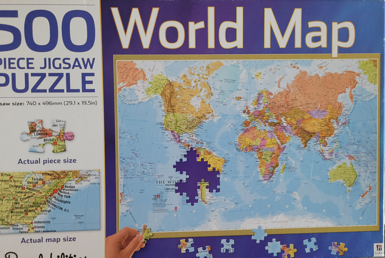 A detailed political world map with a missing jigsaw piece in the Atlantic Ocean and scattered pieces below.