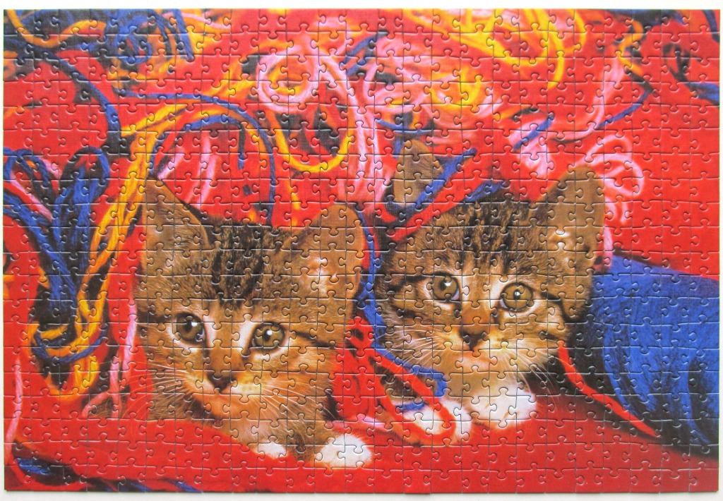 Two tabby kittens nestled amidst a vibrant tangle of colorful yarn on a bright red background.