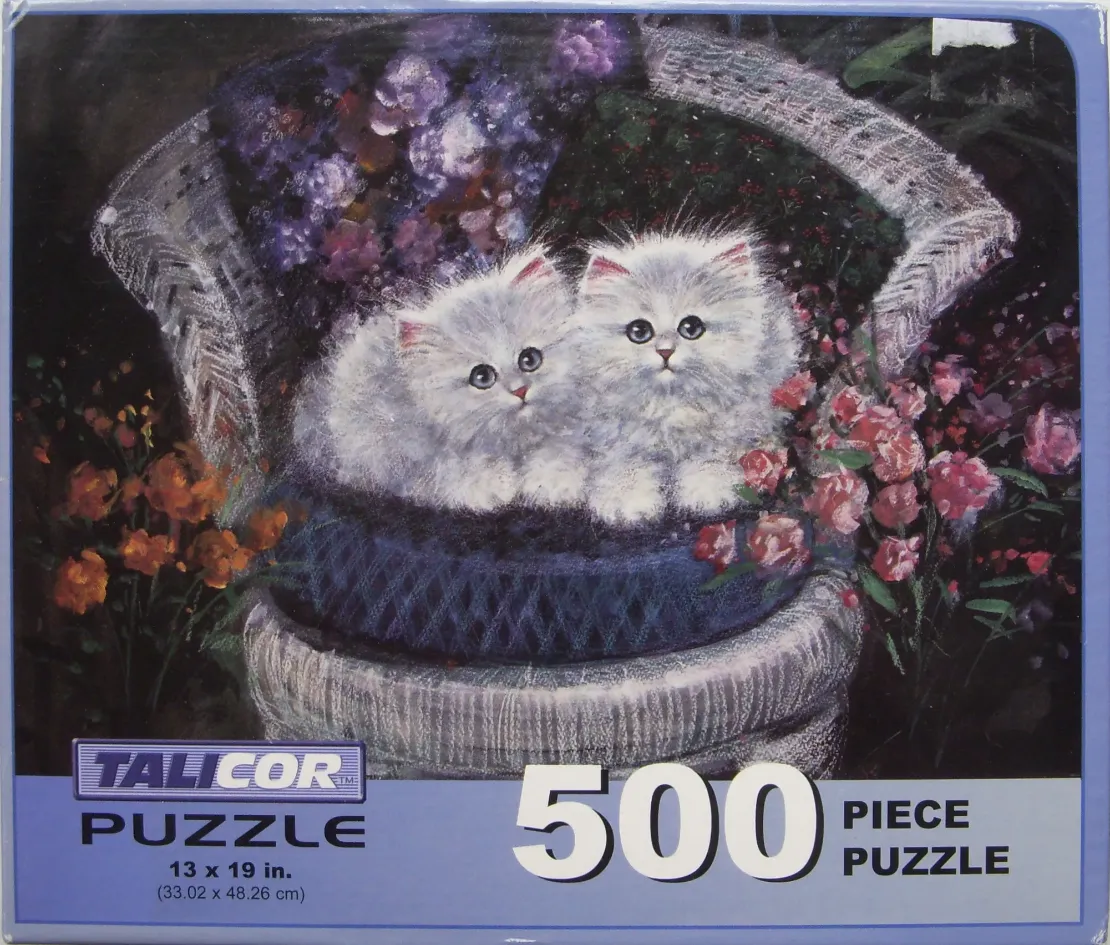 Two fluffy white kittens sitting in a dark blue woven basket on a light-colored wicker chair surrounded by flowers.