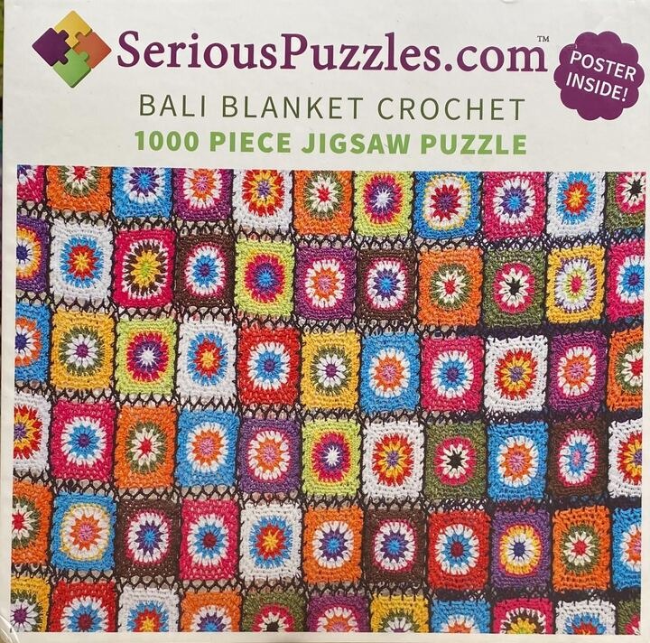 A close-up view of a colorful crochet blanket made of repeating square motifs in a grid pattern.