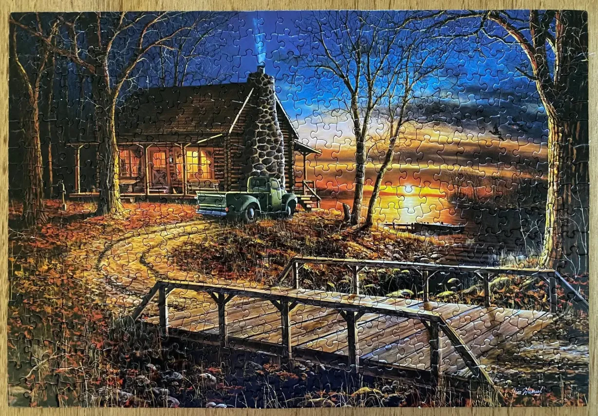 A cozy log cabin at sunset with a vintage truck parked outside near a wooden bridge.