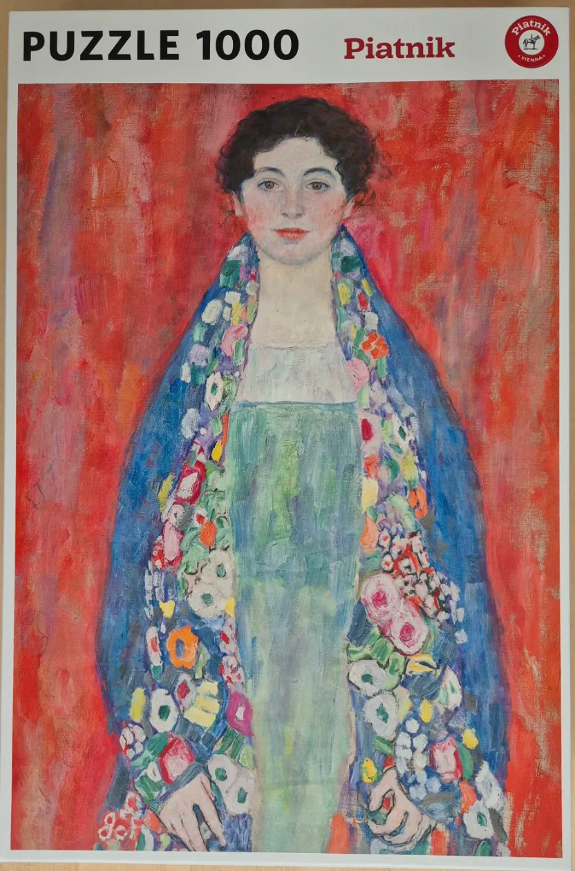 Portrait of a woman with dark hair wearing a vibrant floral shawl against a textured red background.