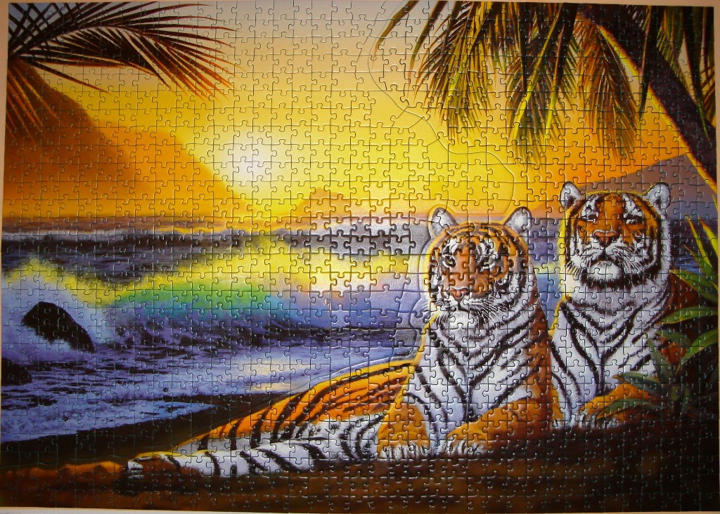 Two tigers resting on a beach at sunset with palm trees framing the scene.