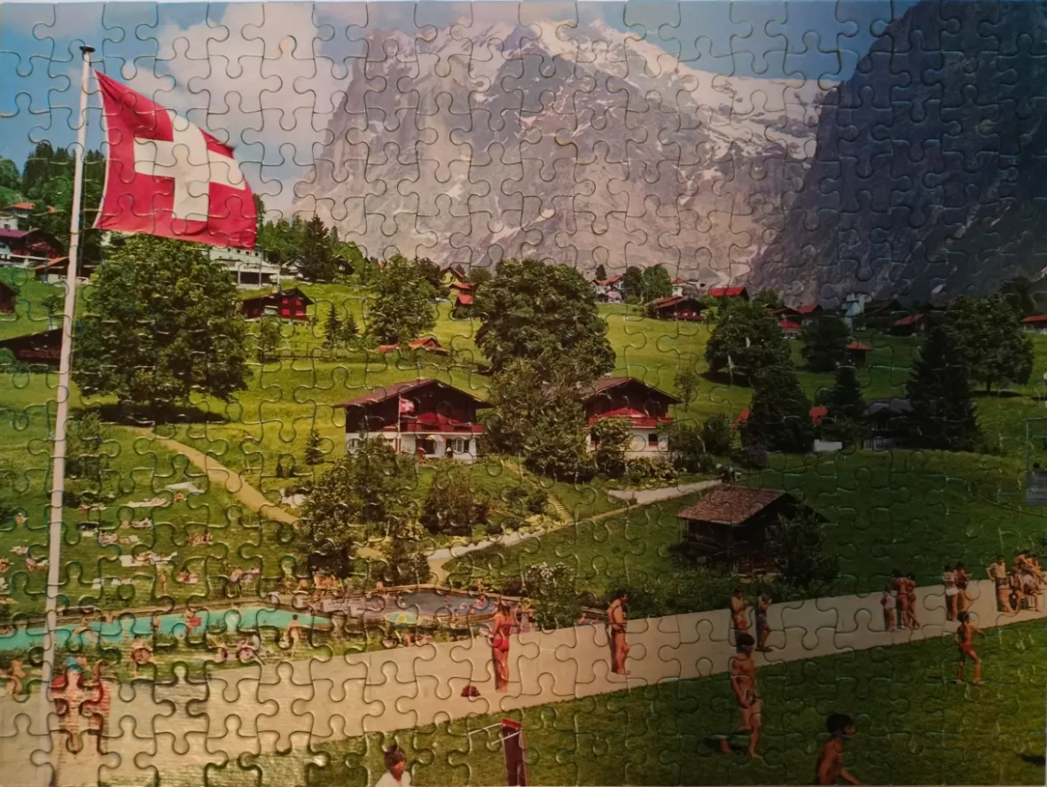 A Swiss flag waves over a sun-drenched valley scene with traditional houses and a swimming pool against mountain peaks.