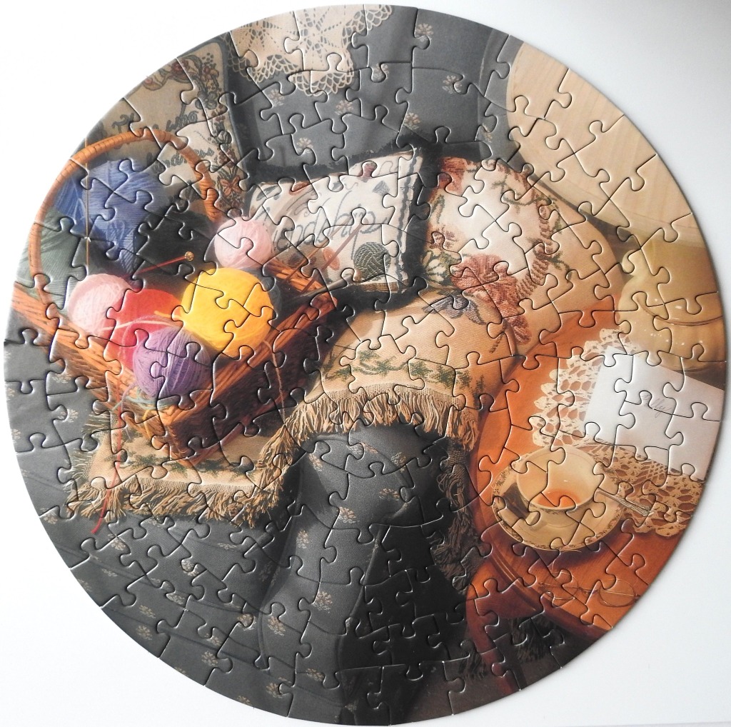 A circular still life image featuring a knitting basket, balls of yarn, a teacup, and lace textiles.