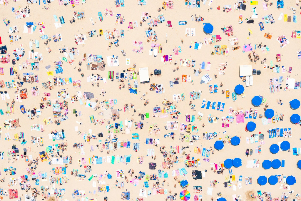 Aerial view of a crowded beach with colorful umbrellas and towels scattered across the sand.