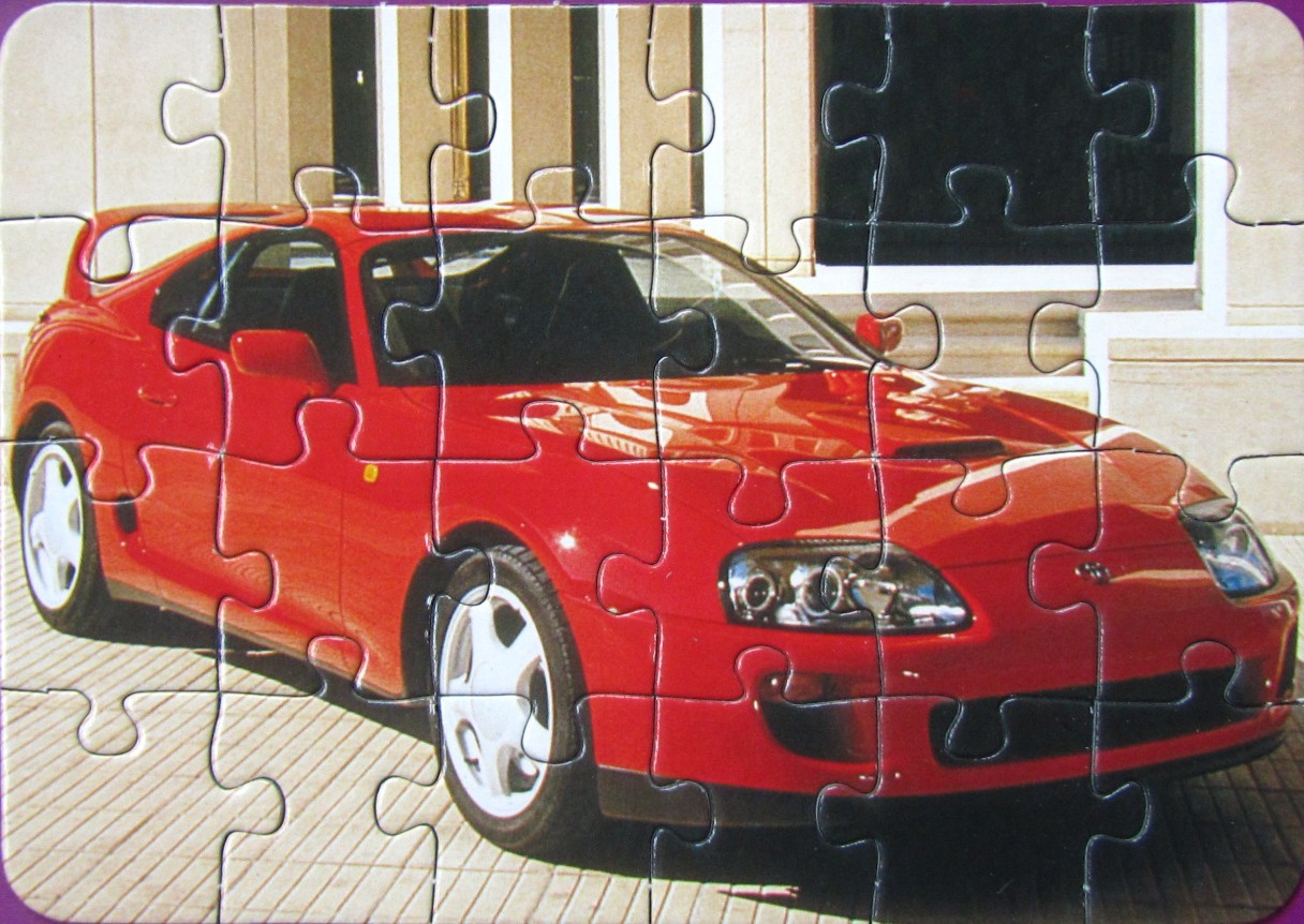 A bright red Toyota Supra sports car parked in front of a modern building with light-colored panels.
