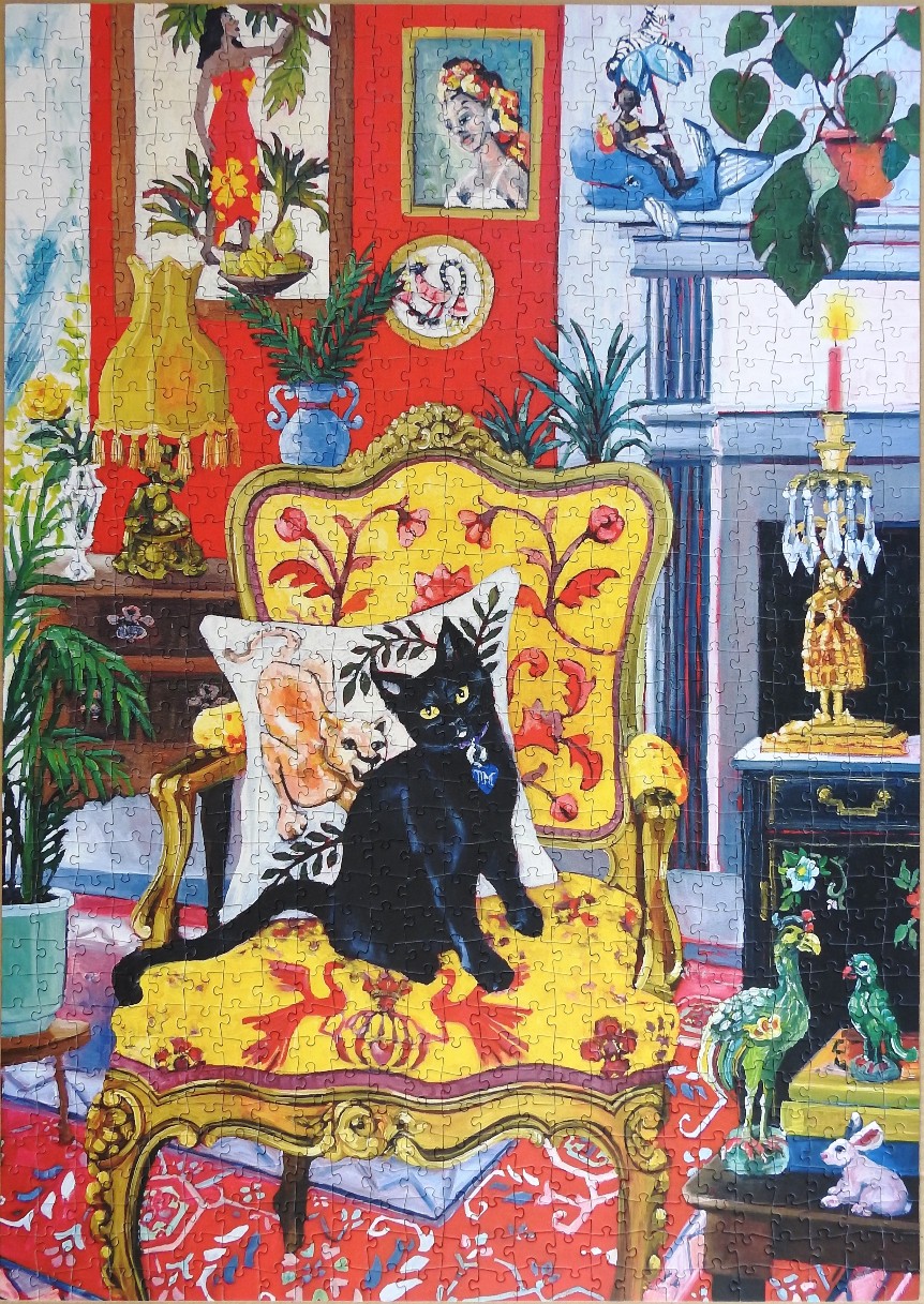 A black cat sits on a yellow patterned armchair in a vibrant, eclectic living room filled with art and plants.
