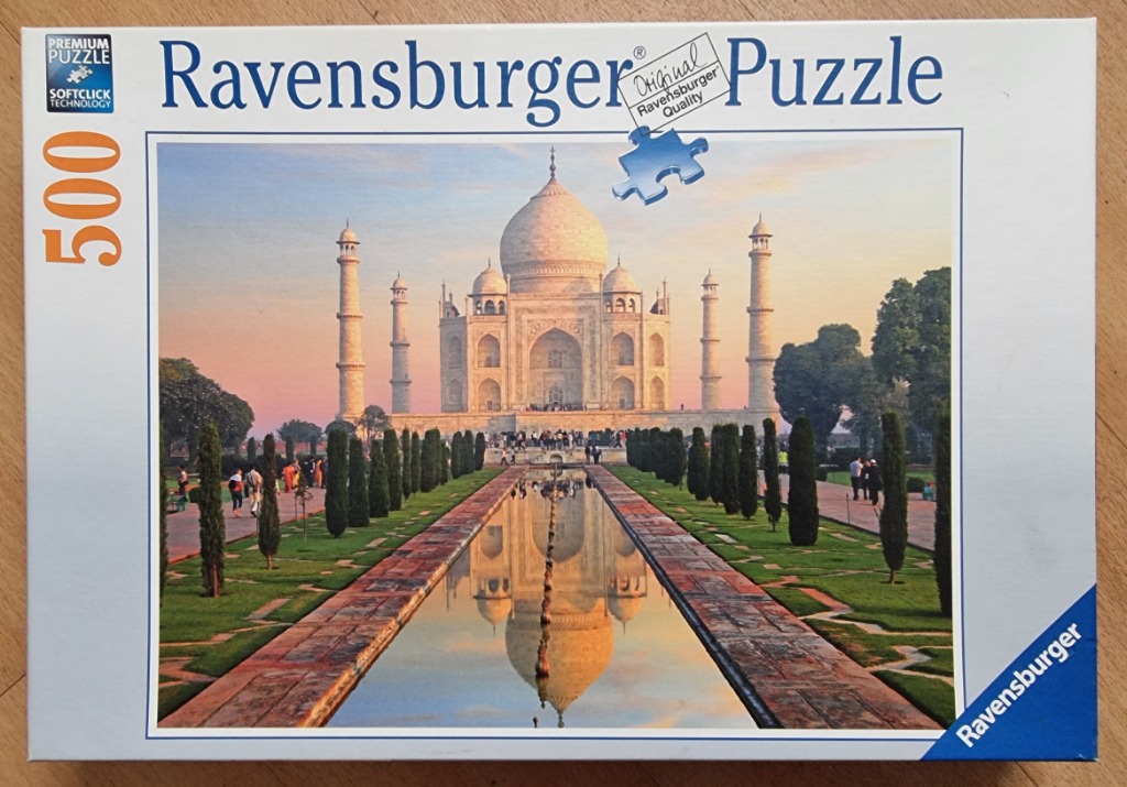 A photograph of the Taj Mahal at sunset, reflecting in a long pool with symmetrical gardens and trees.