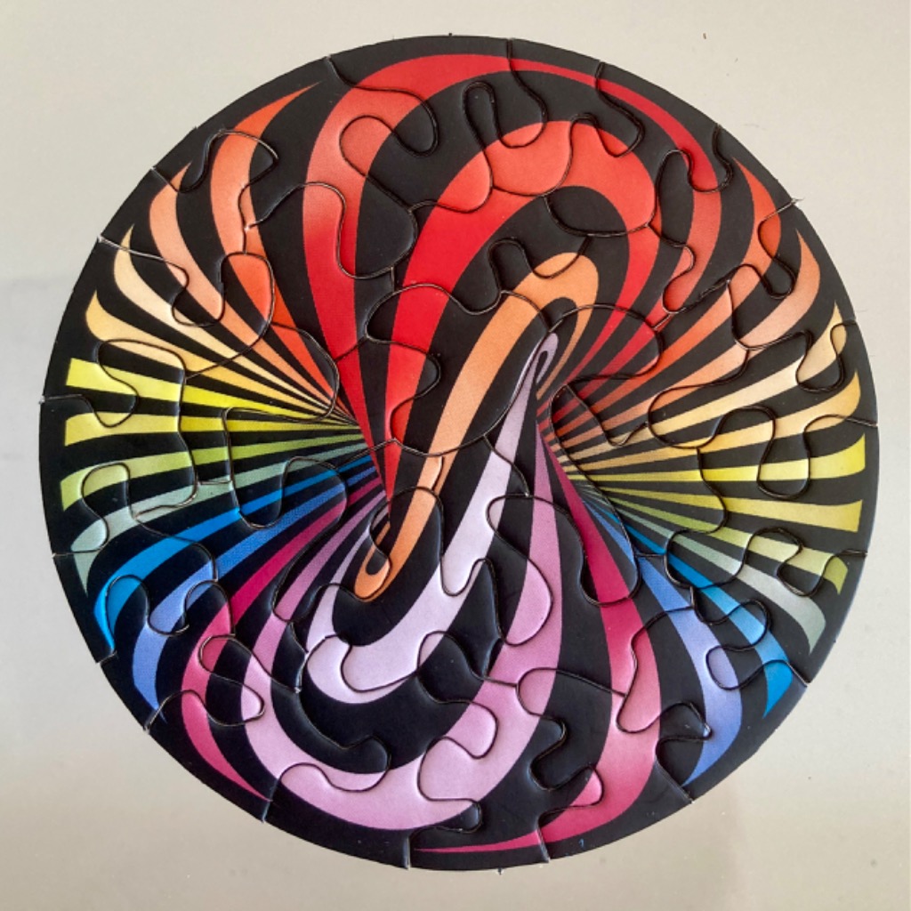 A circular op-art design featuring swirling, rainbow-colored gradients radiating against a black background.