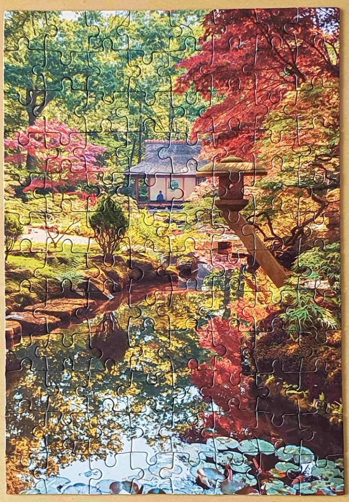 A peaceful Japanese garden in autumn with a traditional stone lantern, a teahouse, and a reflective pond.
