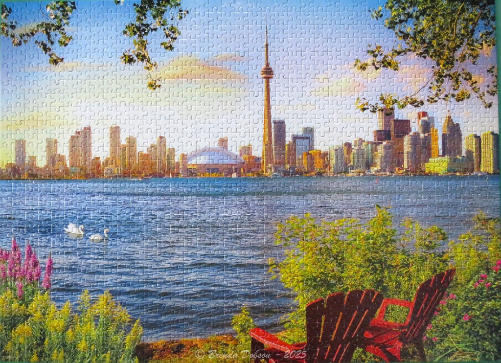 The Toronto skyline across Lake Ontario, viewed from a park with two red Adirondack chairs.