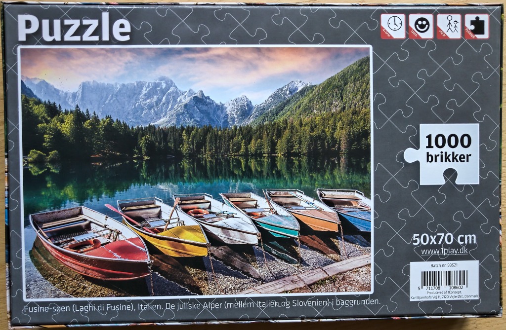 A serene alpine lake scene featuring colorful rowboats moored at the shore with jagged, snow-dusted mountains behind.