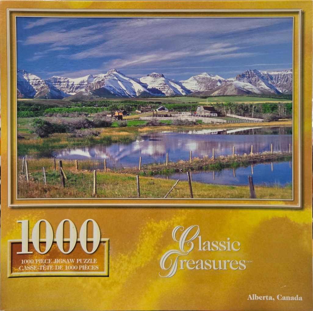 A panoramic landscape of a serene Alberta lake and farmstead set against a backdrop of snow-capped mountains.