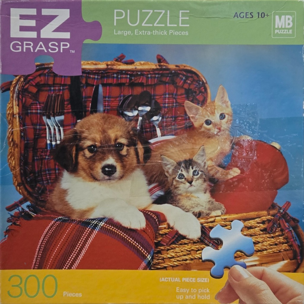 A puppy and two kittens sitting in an open picnic basket lined with plaid fabric.