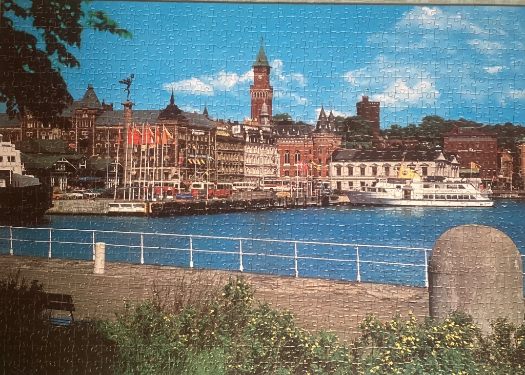 A sunny waterfront view of the Stockholm City Hall with boats and a stone-paved promenade in the foreground.