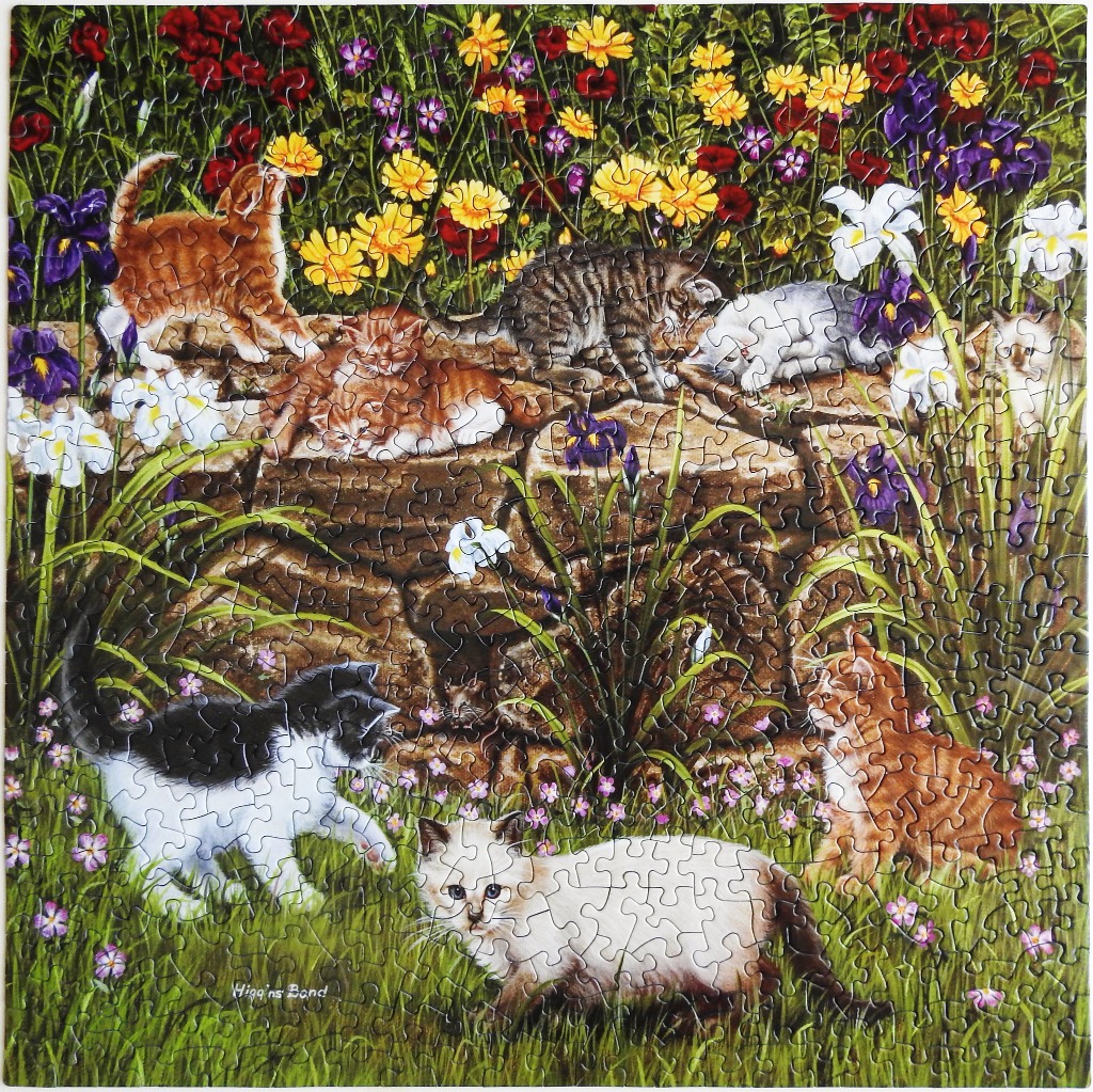 A group of diverse kittens playing and resting in a vibrant flower garden with a stone wall.